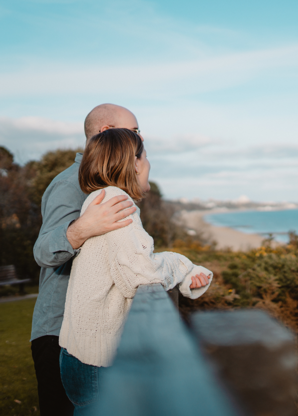 Couple enjoying a scenic beach view on a sunny day, standing close and embracing.