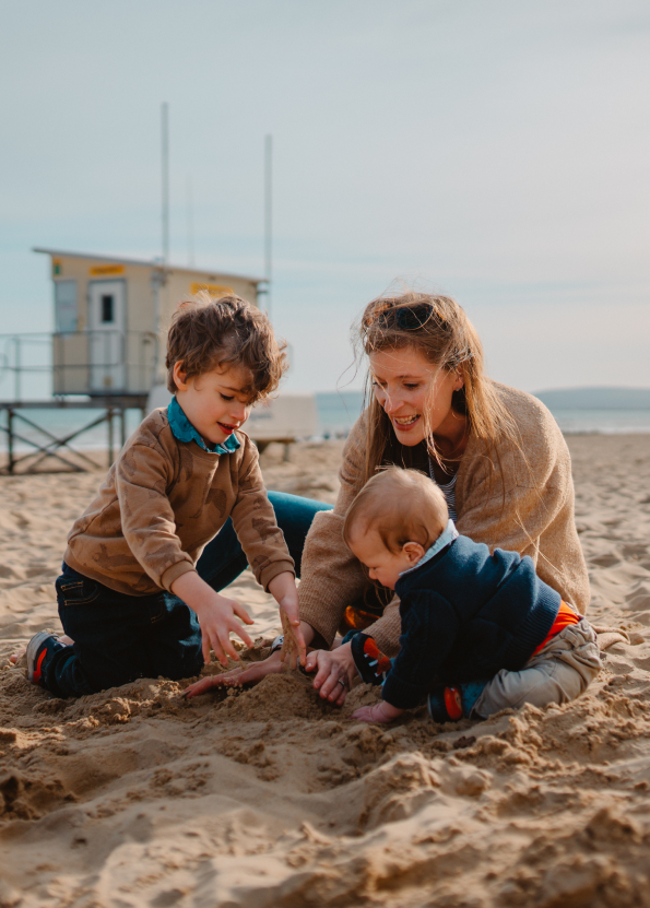 Family playing in the sand at the beach near a lifeguard hut, enjoying a sunny day.