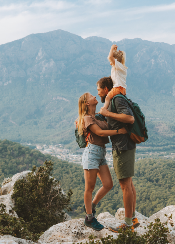 Family hiking in scenic mountains, parents with child on shoulders, enjoying nature and adventure.