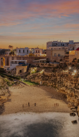 Sunset over Polignano a Mare beach, Italy, with scenic cliffs, historic buildings, and vibrant sky.