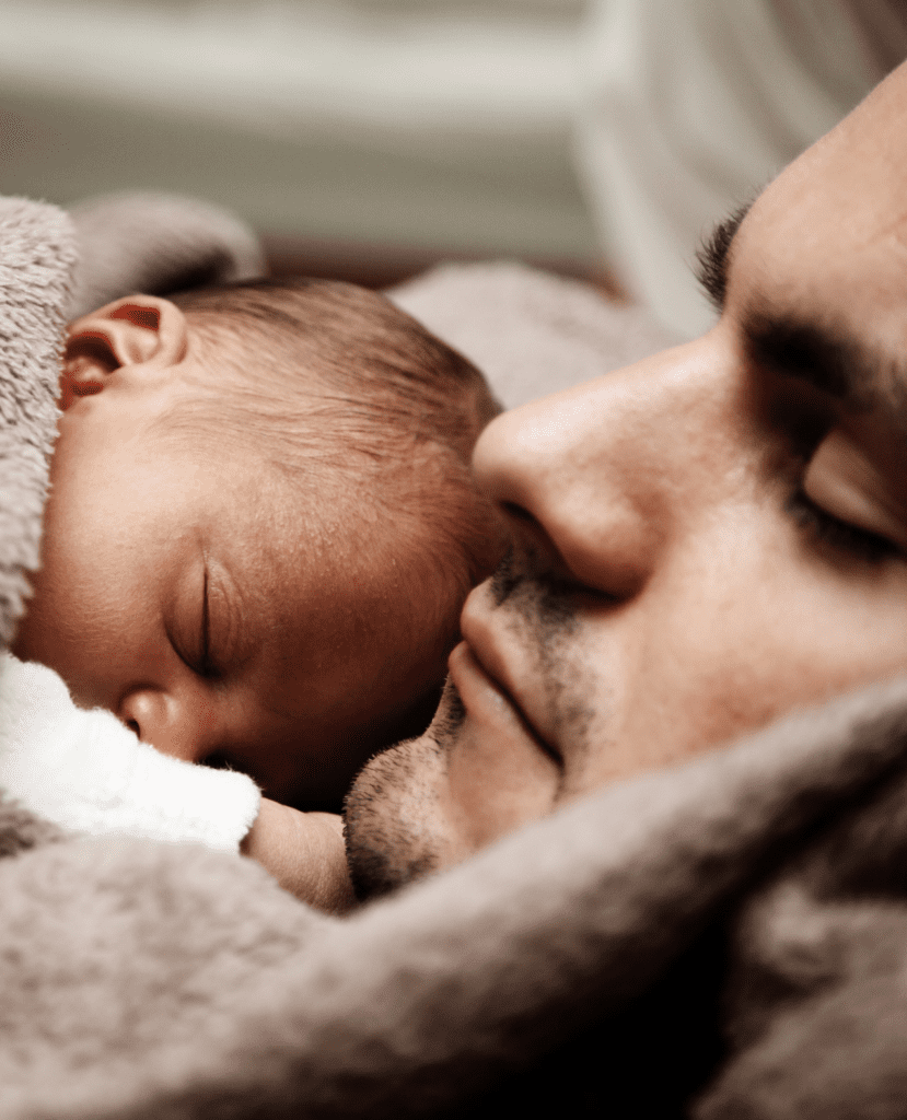 Sleeping father and newborn baby snuggled together under a cozy blanket, capturing a peaceful and tender moment.