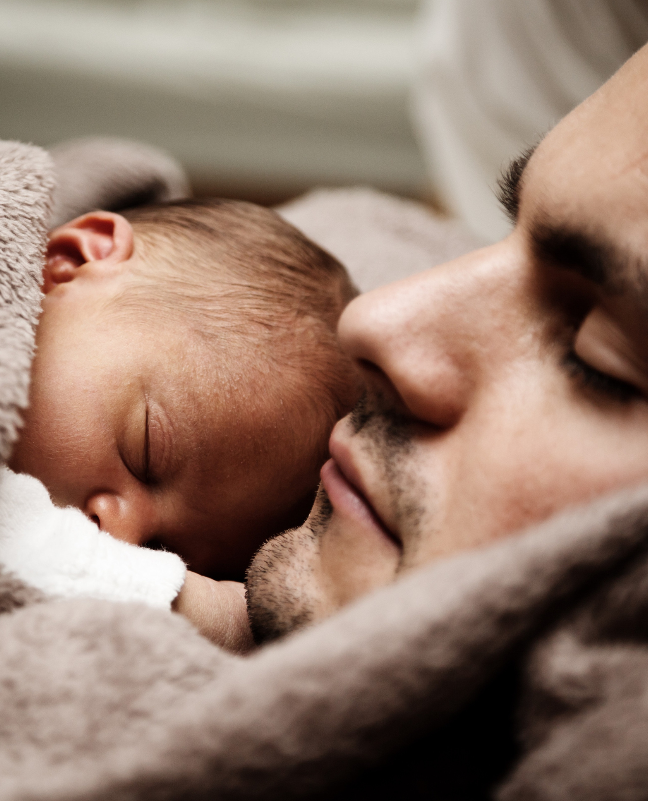 Sleeping father and newborn baby snuggled together under a cozy blanket, capturing a peaceful and tender moment.