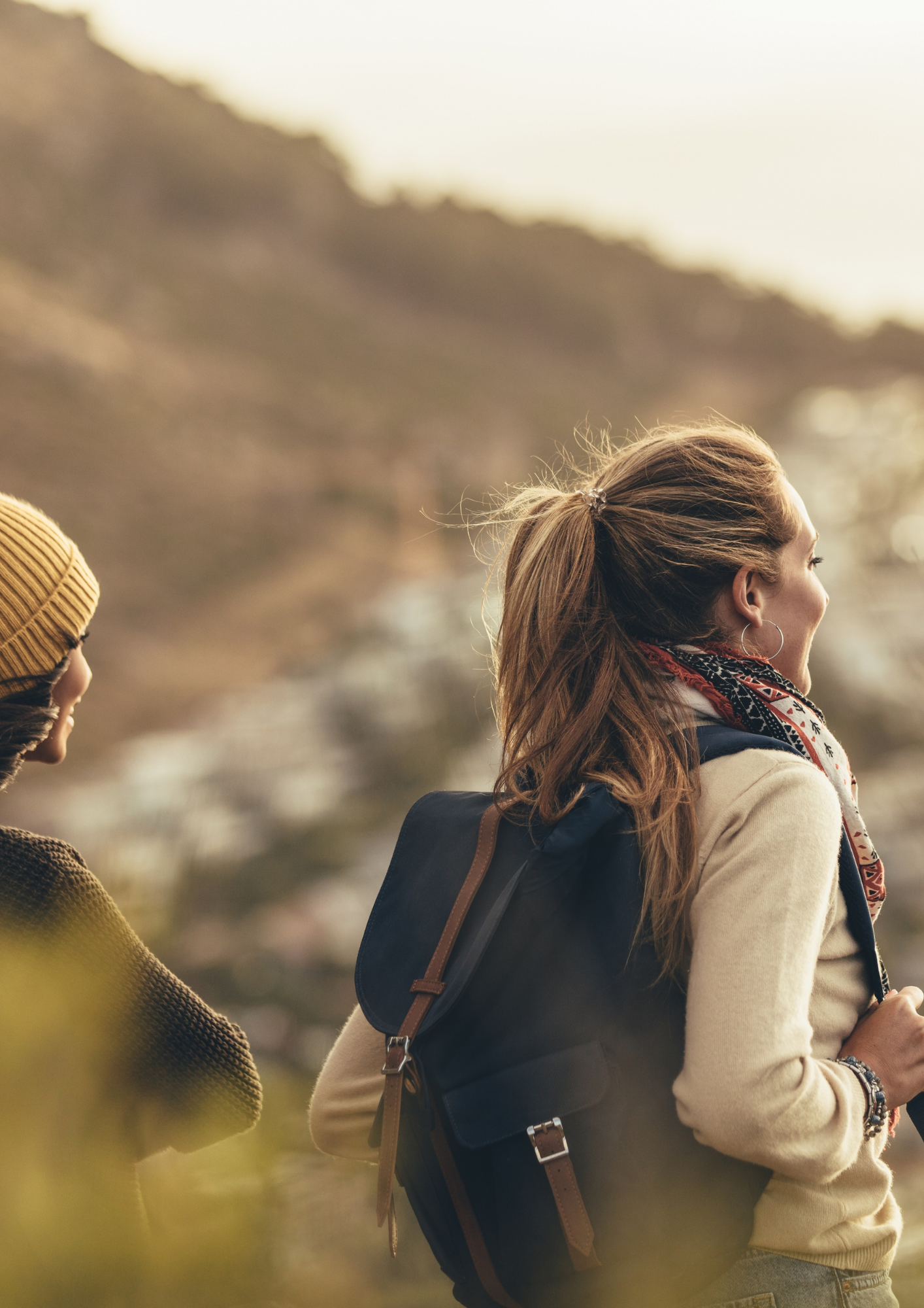 Two women enjoying a hike with backpacks, overlooking a scenic mountain landscape.