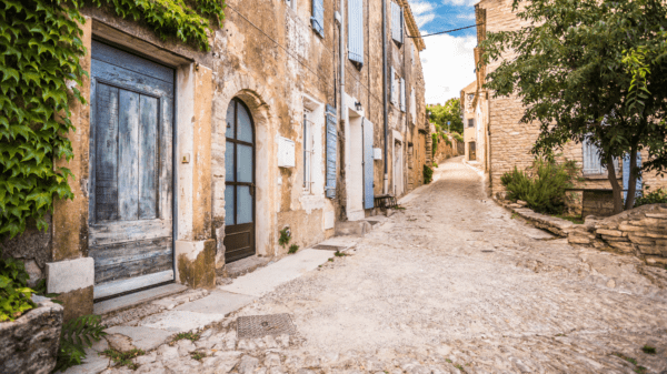 Quaint European village street with stone buildings and blue shutters, perfect for a scenic travel destination.