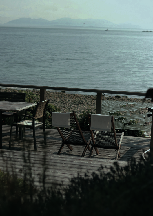 Seaside deck with chairs overlooking tranquil ocean view and distant islands under a clear sky.